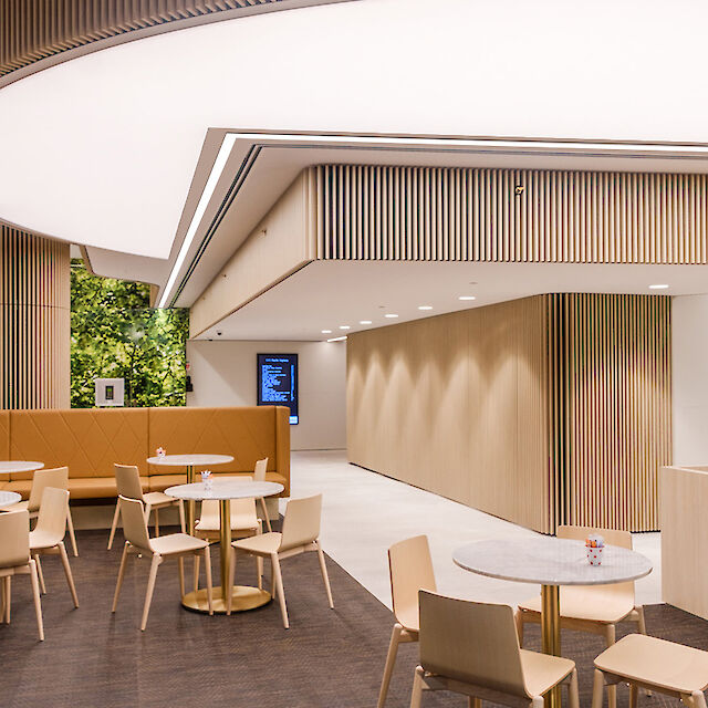 Moderno salón con mesas redondas, paneles de madera e iluminación lineal en el techo.