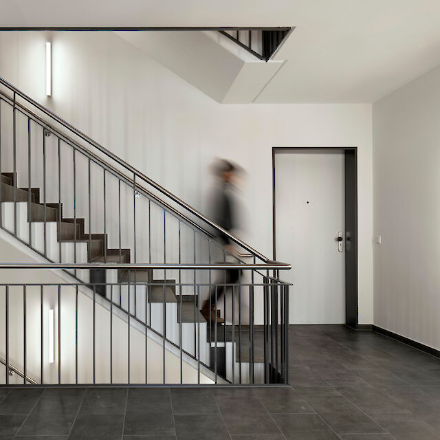 Modern staircase with black banisters, grey tiled floor and vertically mounted LED wall lights
