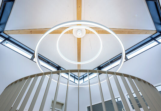 Upward view of two ring-shaped Ringo Star pendant luminaires above a round banister.