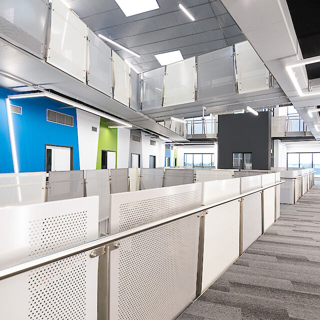 Innenansicht des Chisholm Institute in Melbourne, Australien. Die Aufnahme zeigt einen hellen Gang mit modularen Lichtlinien der Matric-Produktlinie von Lightnet, die an der Decke installiert sind. Der Raum ist mit Metallgeländern und Glaswänden ausgestattet, die in ein minimalistisches Design integriert sind. Große Fenster im Hintergrund lassen Tageslicht herein und betonen die geräumige und offene Architektur.