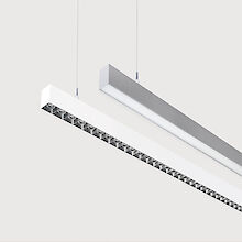 The picture shows a section of two linear pendant luminaires, one with a white and one with a grey surface. The underside of the white luminaire is fitted with a silver-coloured lenticular louvre, with each lens containing a small LED light. The silver-coloured light has a smooth cover. Both lights have a modern design and are suspended from the ceiling on thin cables. The background is grey.