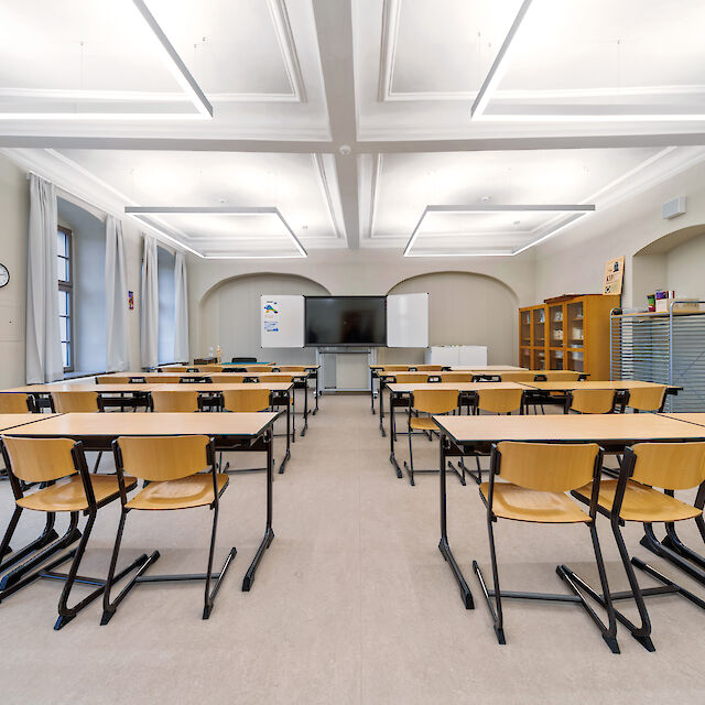 Classroom with wooden chairs, historic ceiling moulds and square Matric pendant luminaires.
