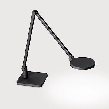 Das Bild zeigt eine moderne, minimalistische Tischleuchte. Die Leuchte ist schwarz und hat einen schlanken, beweglichen Arm, der in zwei Segmente unterteilt ist. Der Leuchtenkopf ist rund und flach. Die Basis der Leuchte ist quadratisch. Die Leuchte steht vor einem hellgrauen Hintergrund.