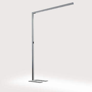 A slender, modern free-standing luminaire with a minimalist design. It has an L-shape and consists of a narrow, metallic pole and a horizontal luminaire arm. The base of the luminaire is rectangular with a U-cut and matches the overall style. The luminaire stands against a neutral grey background. 