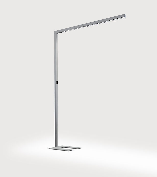 Eine schlanke, moderne Stehleuchte in minimalistischem Design. Sie hat eine L-Form und besteht aus einem schmalen, metallischen Ständer und einem horizontalen Leuchtenarm. Der Fuß der Leuchte ist rechteckig mit einem U-Ausschnitt und passt sich dem Gesamtstil an. Die Leuchte steht vor einem neutralen grauen Hintergrund.