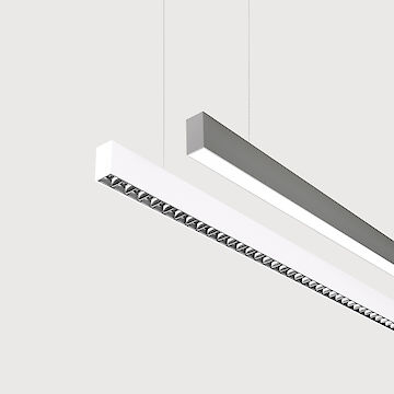 The picture shows a section of two linear pendant luminaires, one with a white and one with a grey surface. The underside of the white luminaire is fitted with a silver-coloured lenticular louvre, with each lens containing a small LED light. The grey luminaire has a smooth cover. Both luminaires have a modern design and are suspended from the ceiling on thin cables. The background is grey.