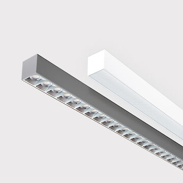 The picture shows a section of two linear surface-mounted luminaires, one with a white and one with a grey surface. The underside of the grey luminaire is fitted with a silver-coloured louvre, with each lens containing a small LED light. The white luminaire has a smooth cover. Both luminaires have a modern design. The background is grey.