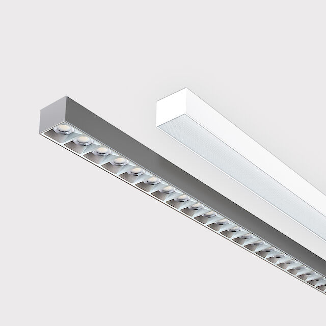 Das Bild zeigt einen Ausschnitt von zwei linearen Anbauleuchten, eine mit weißer und eine mit grauer Oberfläche. Die Unterseite der grauen Leuchte ist mit einem silberfarbenen Linsenraster ausgestattet, wobei jede Linse eine kleine LED-Leuchte enthält. Die weiße Leuchte hat eine glatte Abdeckung. Beide Leuchten sind modern gestaltet. Der Hintergrund ist grau.