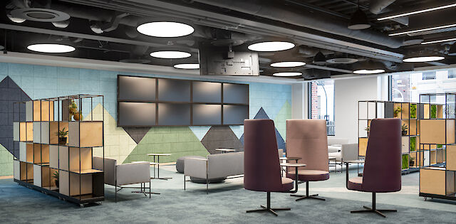 The picture shows a modern, stylish office space with an open, inviting design. The ceiling is fitted with visible pipes and large, round LED luminaires that provide bright lighting. On the walls are colourful, geometric acoustic panels in various shades of grey, blue and green. In the middle of the room are several armchairs and sofas in neutral colours to form small seating groups. Two high, purple armchairs with small round side tables stand out in particular. To the left and right of the picture are open shelves with decorative plants and wooden elements, which organise the room and add decorative accents at the same time.