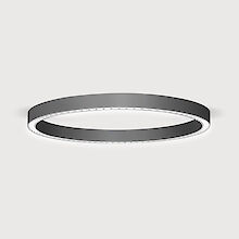 La imagen muestra una moderna lámpara de techo en forma de anillo que emite una luz suave y difusa hacia abajo. La superficie de la luminaria tiene una textura negra mate. El fondo de la imagen es de un gris claro uniforme.