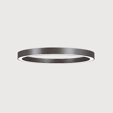 The picture shows a modern, ring-shaped ceiling luminaire that emits a diffuse, soft light downwards. The surface of the luminaire has a matt black texture. The background of the picture is a uniform light grey.