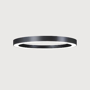 The picture shows a modern, ring-shaped surface-mounted luminaire that emits a diffuse, soft light downwards. The surface of the luminaire has a matt black texture. The background of the picture is a uniform light grey.