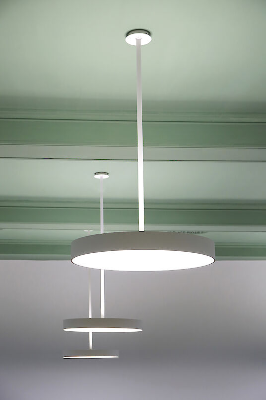 Detailed view of round Basic pendant luminaires in front of a green ceiling.