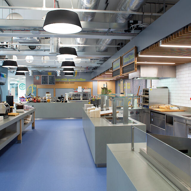 Modern canteen with open cooking stations, blue floor coverings and black Beam Me Up pendant luminaires on the ceiling.