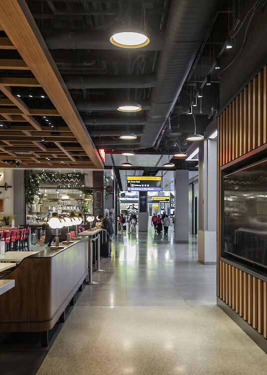 Vista interior del Moynihan Food Hall con vistas a la estación de tren, zonas de asientos y luminarias suspendidas Beam Me Up.