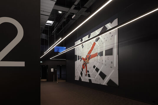 Dark cinema hallway with large numbers, film graphics and linear Liquid Line pendant luminaires on the ceiling.