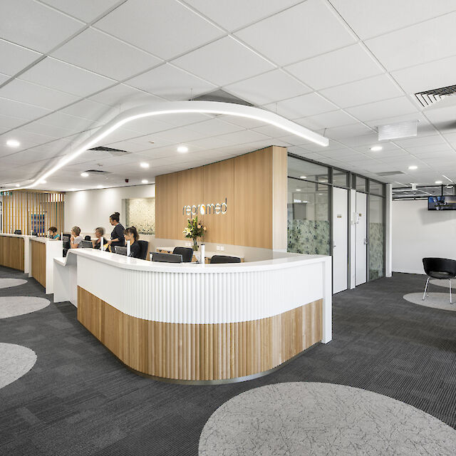 Reception area with reception desk, wood and white accents and a curved light line.