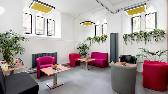 Seating area with colourful armchairs, tables, plants and square pendant lights with acoustic panels