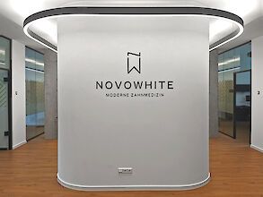 Reception area of a dental practice with direct/indirect linear LED ceiling lighting and ‘NOVOWHITE Modern Dentistry’ logo.