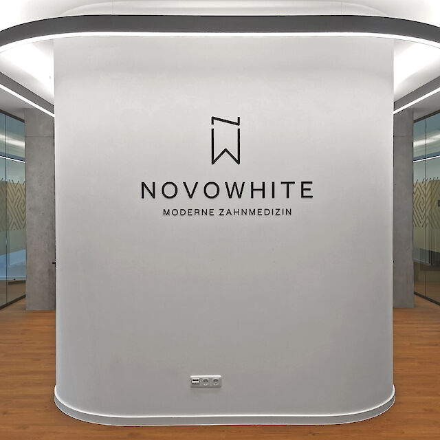 Reception area of a dental practice with direct/indirect linear LED ceiling lighting and ‘NOVOWHITE Modern Dentistry’ logo.