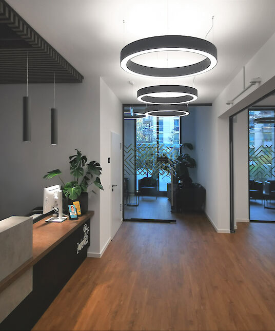 Reception area with wooden floor, round Ringo Star pendant luminaires and green waiting area in the background.