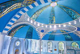 Interior view of the Ulu Mosque with blue dome, ornate ornaments and ring-shaped Ringo-Star pendant luminaire.