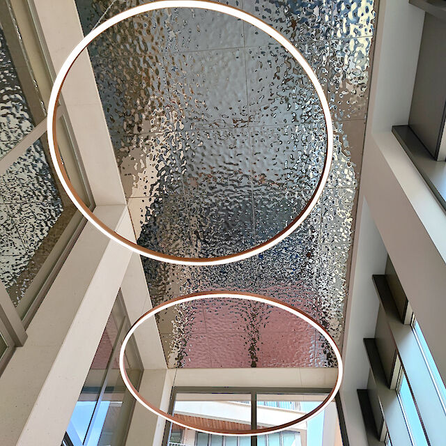 Dos anillos de LED iluminados delante de un techo estructurado en un moderno edificio inundado de luz