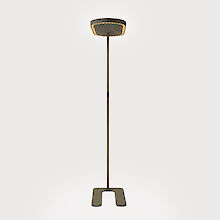 La imagen muestra una moderna lámpara de pie de diseño sencillo y minimalista. La luminaria consta de un marco negro delgado que termina en la parte superior con una cabeza de luminaria plana y redonda. La cabeza de la luminaria está formada por una rejilla lenticular y un tejido acústico. La base de la luminaria tiene forma de U que le proporciona estabilidad. El diseño general es elegante y funcional, adecuado para un interior contemporáneo.
