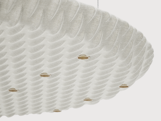 Close-up of a large, round acoustic pendant luminaire. The surface of the luminaire has a structured, wave-like texture and is kept in a light colour. Several small, evenly distributed points of light are integrated into the design and provide discreet lighting.
