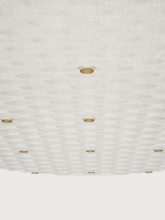 Close-up of an acoustic pendant luminaire. The surface of the luminaire has a structured, wave-like texture and is kept in a light colour. Several small, evenly distributed points of light are integrated into the design and provide discreet lighting.