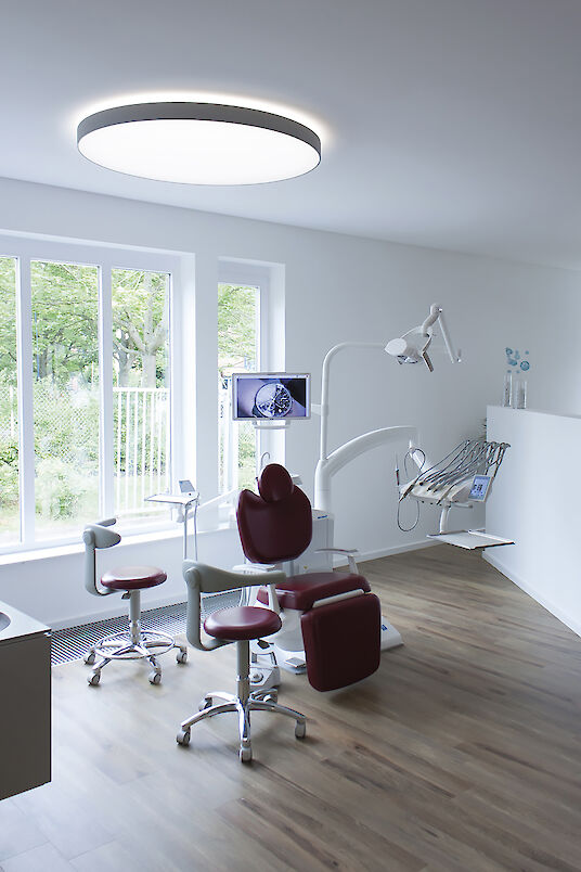Salle de soins lumineuse avec fauteuil dentaire, grande fenêtre et luminaire Basic circulaire apparent.