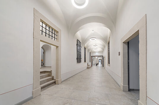 Long hallway with vaulted ceiling, stone floor and ring-shaped Ringo Star pendant luminaires.