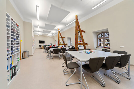 Classroom with group tables, wooden elements, acoustic panels and linear Vision pendant luminaires.