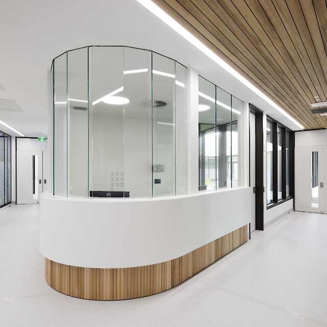 Bright hallway with round glass reception desk, wooden ceiling and linear lighting with recessed luminaires