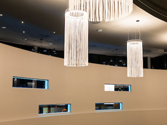 Round wall with narrow window openings and hanging Ringo Star Chandelier pendant luminaires in the foreground.