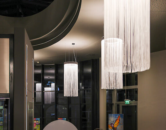 Entrance area with large Ringo Star Chandelier pendant luminaires in front of a high glass façade and emergency exit door.