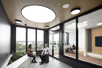 Room with large round recessed lighting, wooden ceiling, glass walls and seating area with plants.