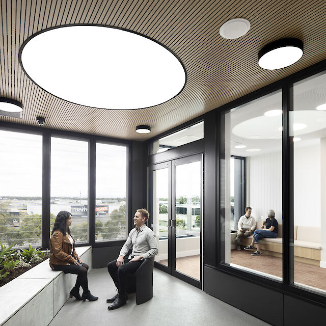 Room with large round recessed lighting, wooden ceiling, glass walls and seating area with plants.