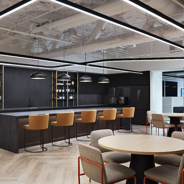 Office kitchen with dark counter, bar stools, round tables and striking ceiling lighting with Liquid Line light lines.