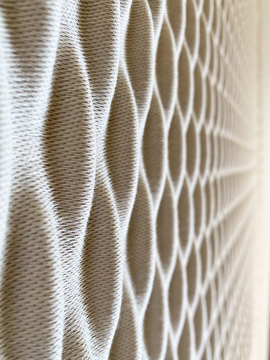 Primer plano de un material acústico estructurado con un patrón de nido de abeja y una superficie textil suave.