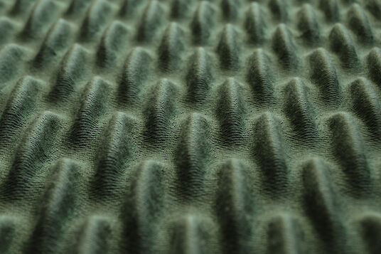 Primer plano de un material acústico de color verde oscuro con una estructura de ondas regular y tridimensional.