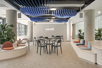 Bright seating area with round benches, black chairs, blue acoustic elements and basic pendant luminaires.