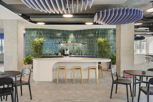 Canteen with green tiled back wall, white counter, wooden stools and round basic pendant luminaires.