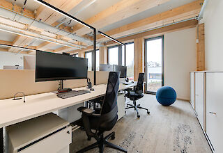Moderne Büroarbeitsplätze mit ergonomischen Stühlen, großen Monitoren und natürlichem Lichteinfall durch bodentiefe Fenster.
